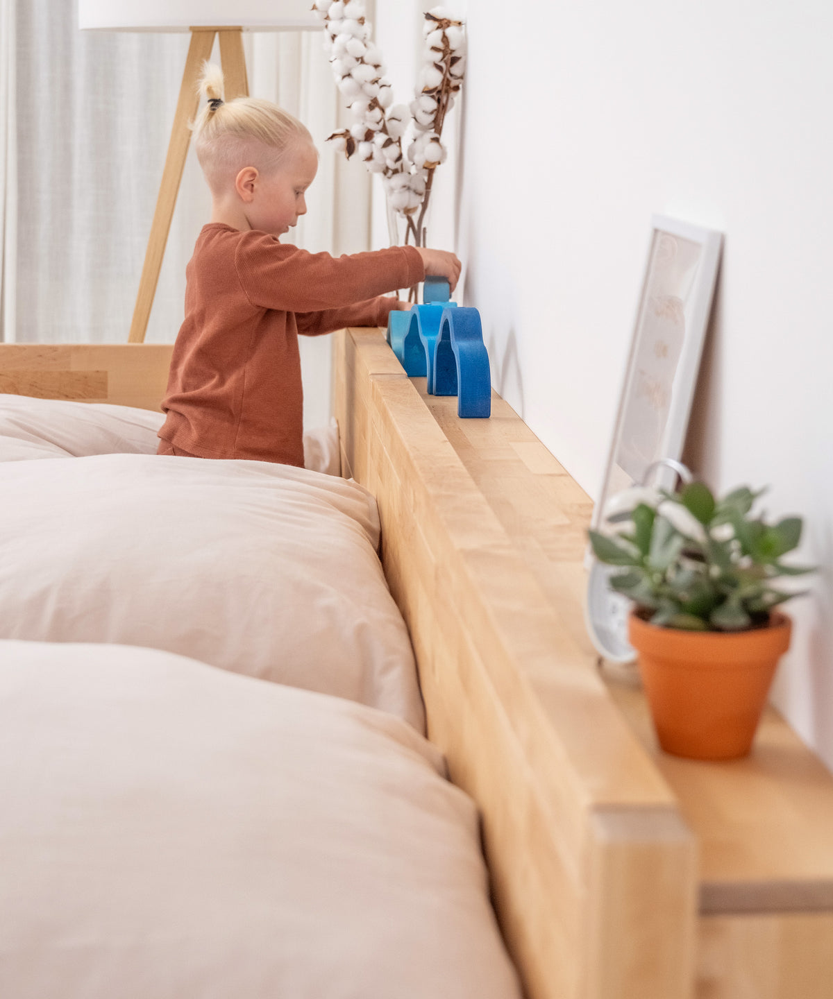 Kind spielt mit Holzspielzeug auf Ablage hinter Bett.