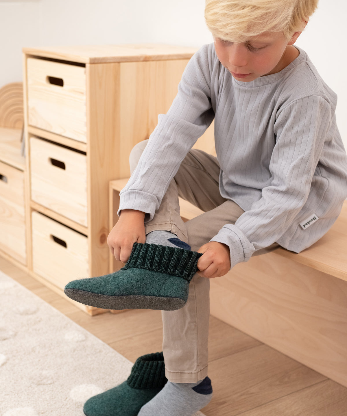 Junge zieht Hüttenschuhe mit Strickbündchen in Waldgrün an.