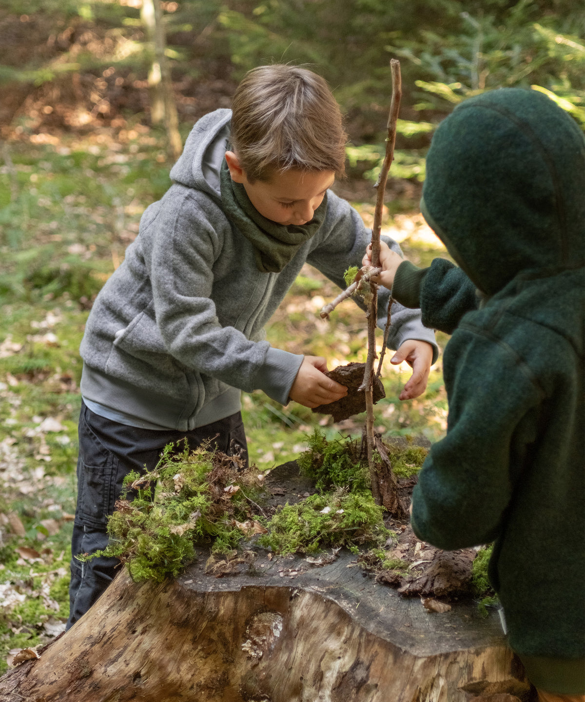 Zwei Kinder mit Wollfleecejacken spielen im Wald.