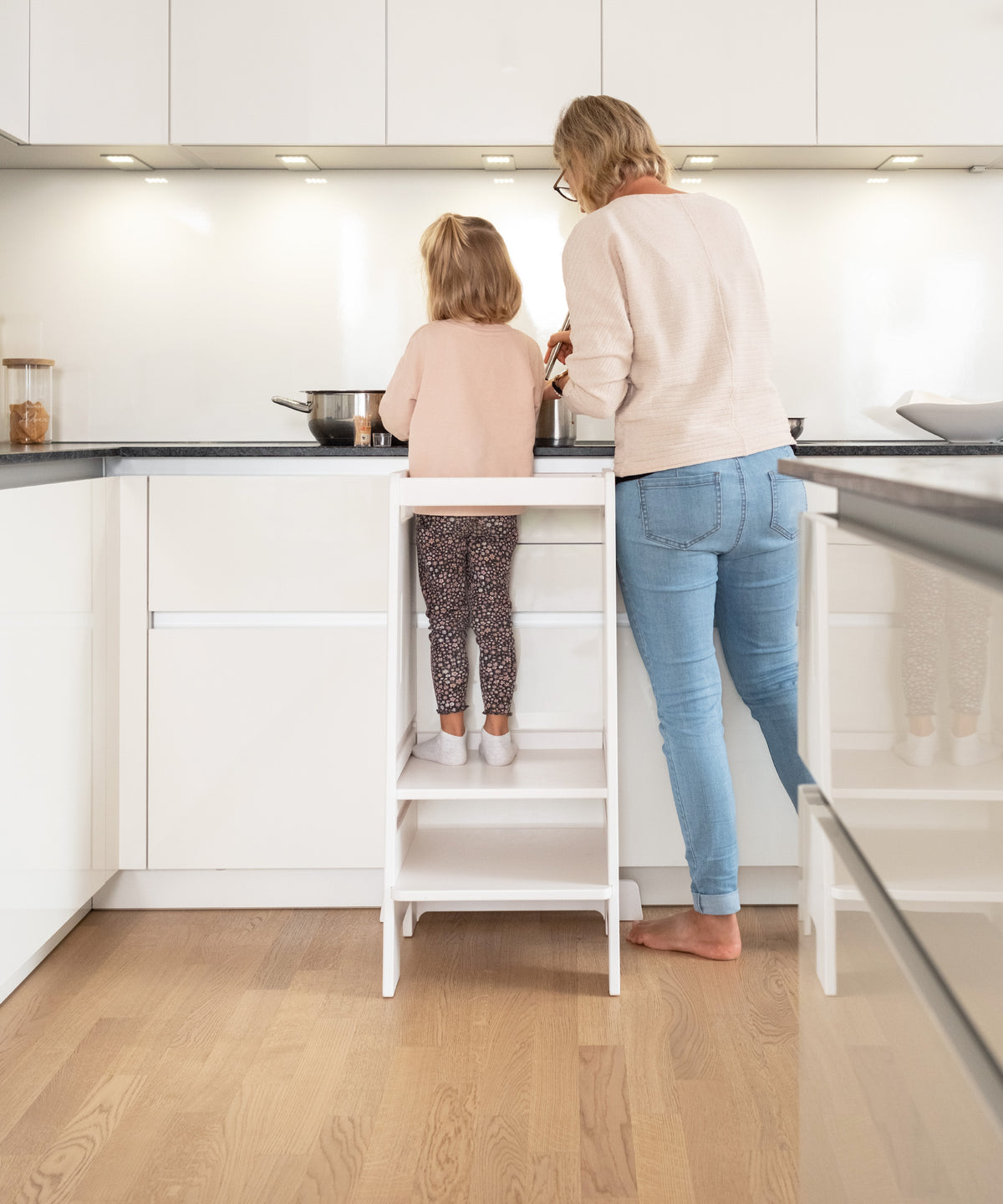 Ein Kind steht auf dem Lernturm und hilft beim Kochen an der Küchenzeile.