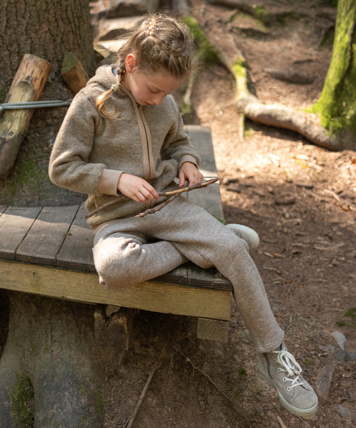 Mädchen sitzt im Wald und spielt mit Stöcken.