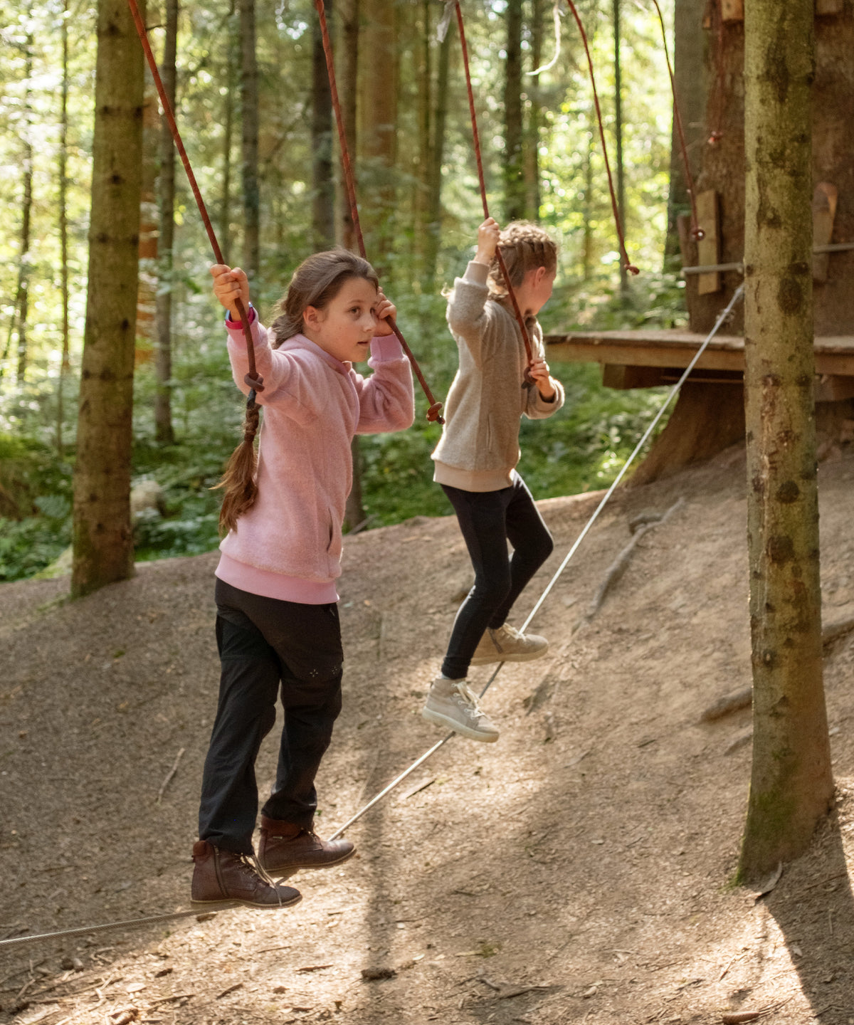 Kinder mit Wollfleecejacken auf Kletterparcours im Wald.