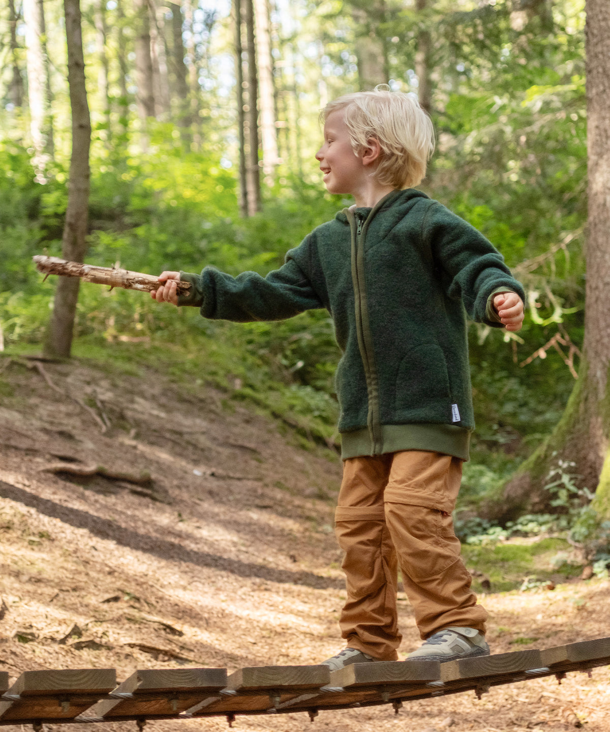 Junge mit Wollfleece-Jacke Waldgrün spielt im Wald.