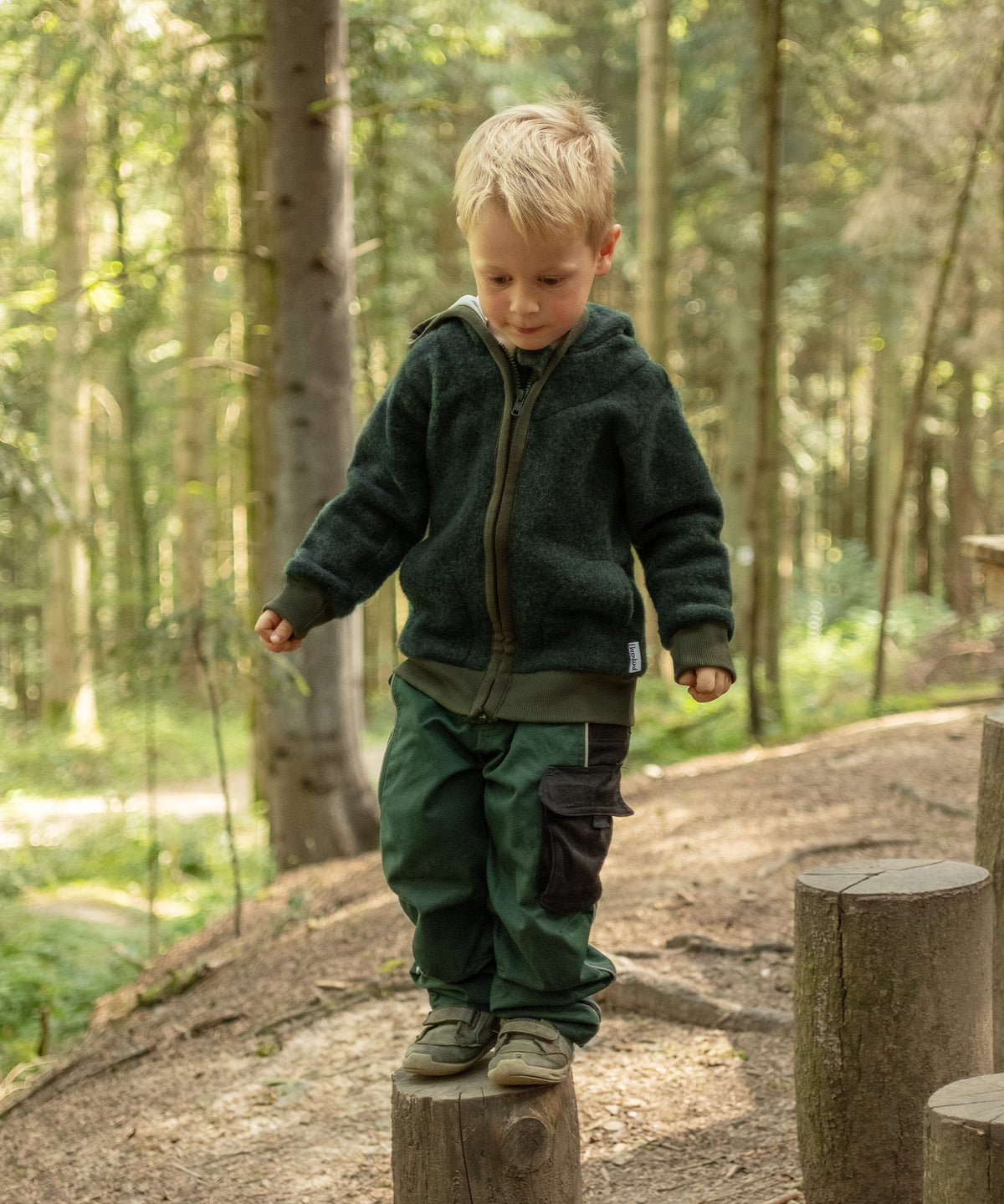 Junge mit atmungsaktiver Wollfleecejacke spielt im Wald.